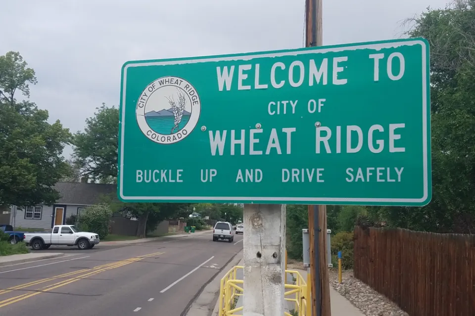 A road sign reads "Welcome to City of Wheat Ridge Buckle Up and Drive Safely"